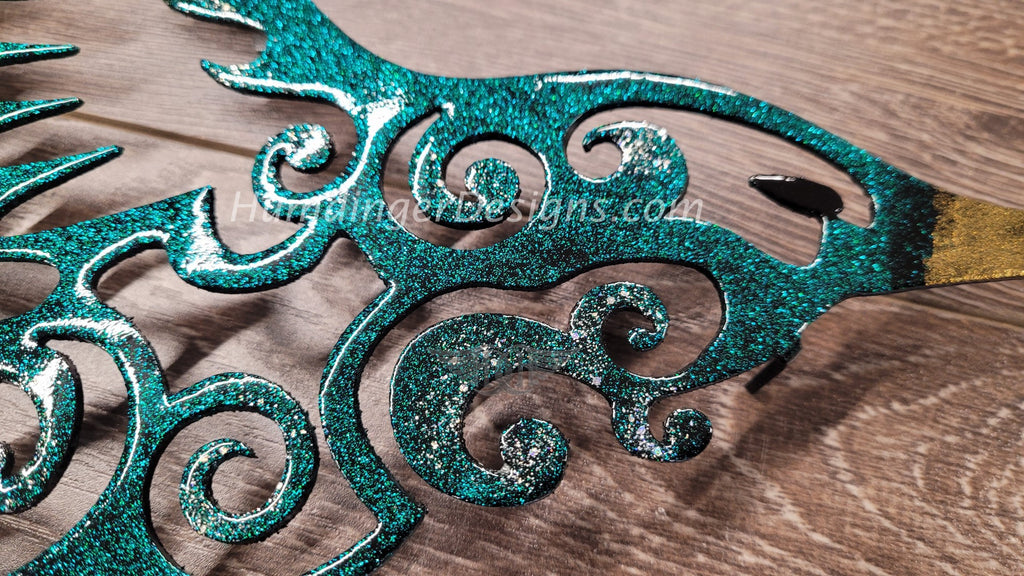 Hand-painted metal hummingbird art featuring intricate swirl designs in vibrant teal glitter finish. Premium quality wall decor.